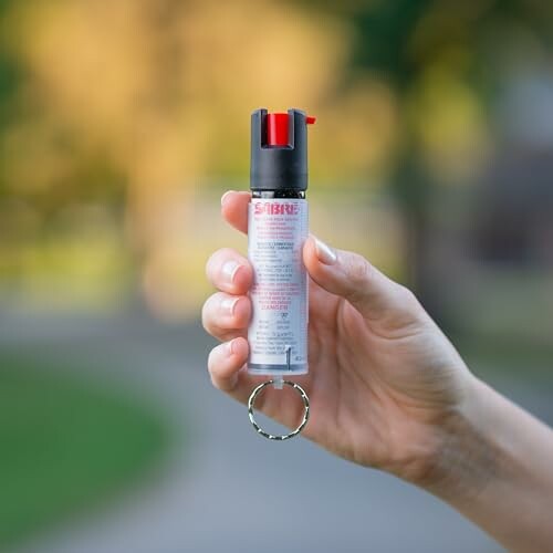 Person holding a small pepper spray canister with a keychain.