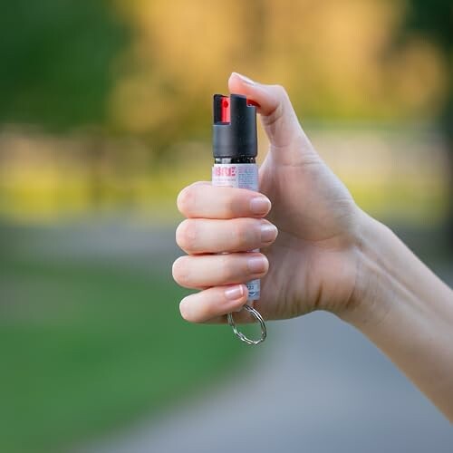 Hand holding a can of pepper spray outdoors.